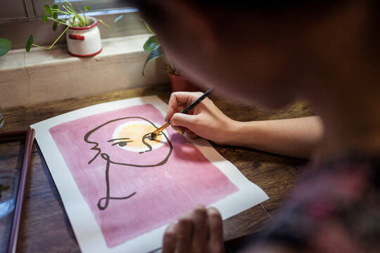 Closeup view of crop unrecognizable female artist creating picture with paint and brush on canvas in workshop