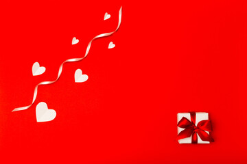 Valentine's Day composition. White paper hearts and small white gift box with red ribbon on red background in flat lay style. Valentines day concept