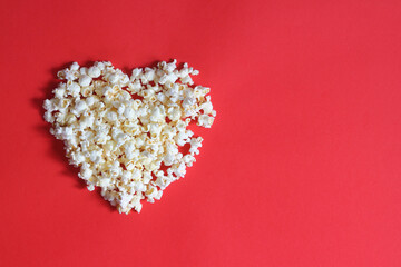 Love cinema concept of popcorn. Heart shaped white fluffy popcorn on red background with empty space for text. Valentine days concept. 	
