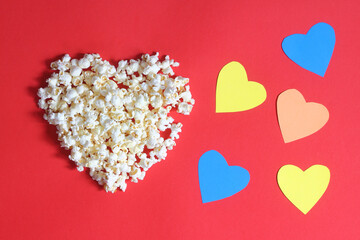 Love cinema concept of popcorn. Heart shaped white fluffy popcorn on red background with empty space for text. Valentine days concept. 	
