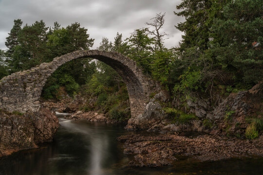 Scenery of Old Pack Horse Bridge over calm river under cloudy sky in Scotland