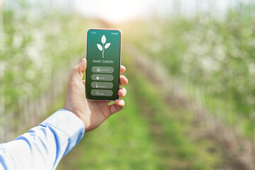 Agronomist holding mobile phone with SMART GARDEN app, checking temperature, humidity and other...