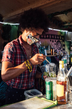 African American male barkeeper in protective mask garnishing cocktail with slice of fresh lime while preparing drink at counter of beach bar