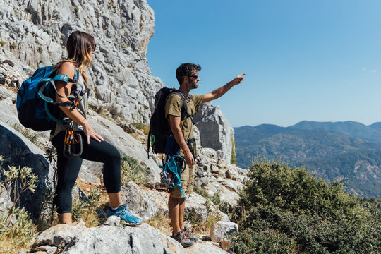 Side view of man and woman with backpacks and safety equipment standing on trail admiring rocky mountain slope