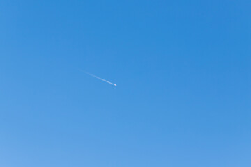 Blue sky without clouds. An airplane can be seen in the sky, followed by a flight trail.