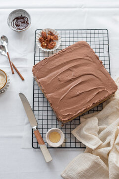 High angle of homemade chocolate square shaped cake arranged on whit table with napkin and various utensils