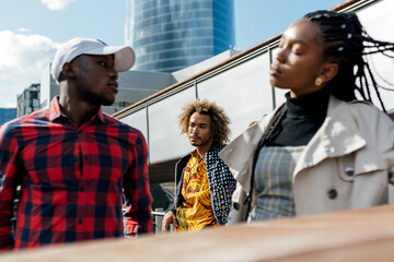 Unhappy young black man suffering from unrequited love while girlfriend having serious conversation with other guy on city street