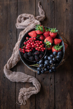 Top view of bowl with various healthy fruits and berries placed on table near old towel in rustic kitchen