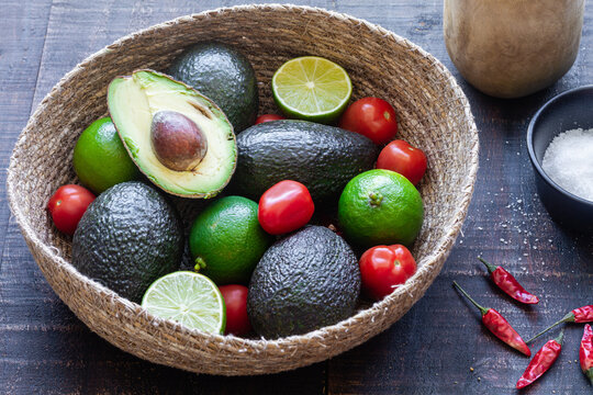 Top view bowl with fresh avocado and lime with tomatoes placed on wooden table with spices for traditional Mexican guacamole recipe
