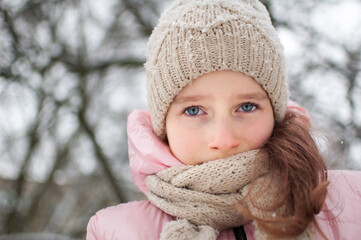 Sad child girl in warm knitted winter clothes spent time outdoors and got frozen.