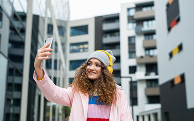 Fototapeta premium Young woman with smartphone making video for social media outdoors on street.