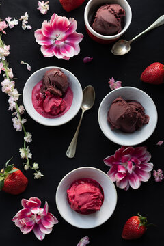 From above of strawberry and chocolate ice cream scoops arranged on black background with flowers and berries