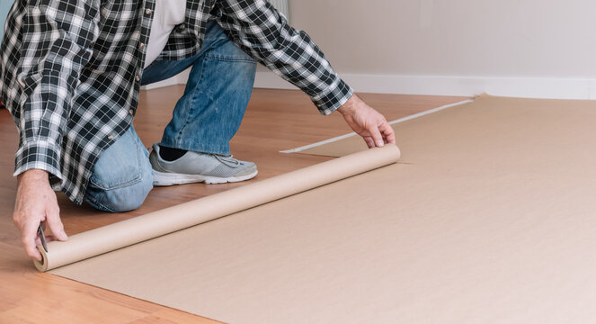 Crop unrecognizable male painter covering floor with craft paper while preparing room for painting and renovation