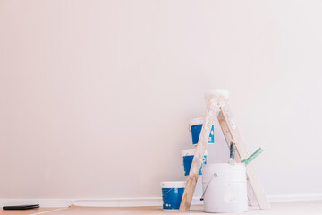 Dirty wooden ladder and buckets with paint and rollers placed in room for renovation