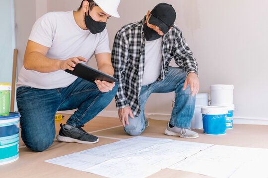 Male painters in protective masks examining paper sketches while preparing for renovation in modern flat