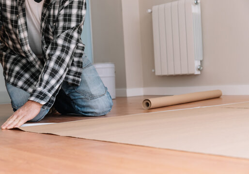 Unrecognizable male painter sticking craft paper to floor with tape while preparing modern room for painting and renovation