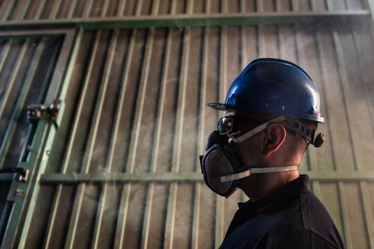 Low angle side view of male worker in hardhat and respirator during accident in smoked workshop