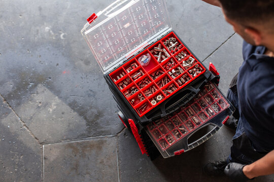 Top view of anonymous mechanic in gloves sorting various nuts and screws inside tool box during work in garage