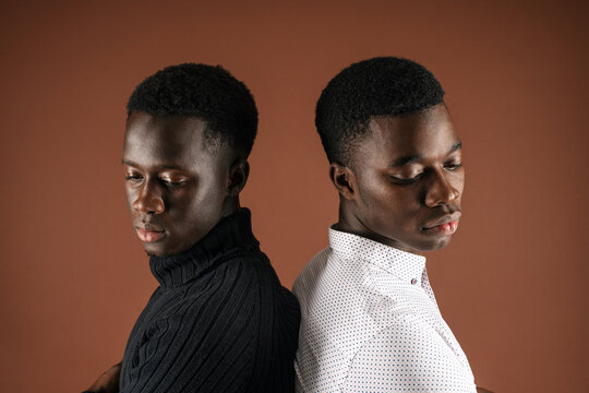 Side View Of Determined African American Male Friends Standing Back To Back With Crossed Arms On Brown Background