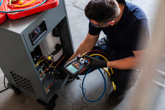 Male mechanic in goggles and gloves using voltage tester on modern machine during work in workshop