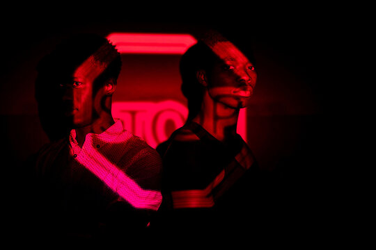 Side view of African American males standing in dark studio illuminated by red neon light of projection of stop road sign