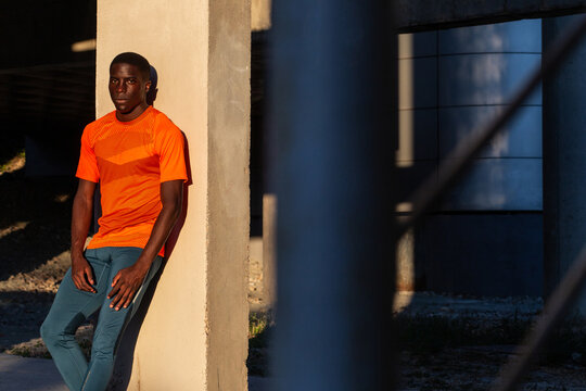 Exhausted African American male runner leaning in column in city while relaxing after active workout and looking at camera