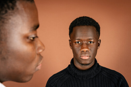 Back view of ethnic man standing in studio with African American male looking confidently at camera on brown background