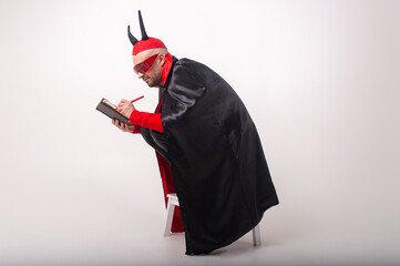 Caucasian man in red sunglasses and halloween costume with pen and notebook over white studio...