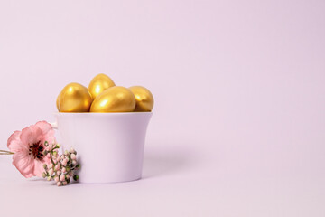 Easter composition of golden decorative eggs in a porcelain cup and a flower. Selective focus, copy space.