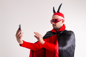 Unusual caucasian man in red sunglasses, black red halloween costume and hat with devil horns...