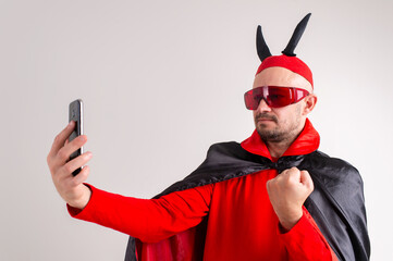 Unusual caucasian man in red sunglasses, black red halloween costume and hat with devil horns...