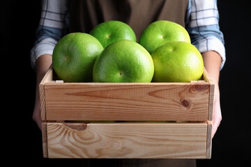 Woman holding wooden crate with sweetie fruits on black background, closeup