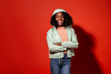 Modern ethnic woman with Afro hairstyle wearing casual denim with jacket and hood on vivid red background