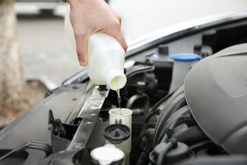 Man filling car radiator with antifreeze outdoors, closeup