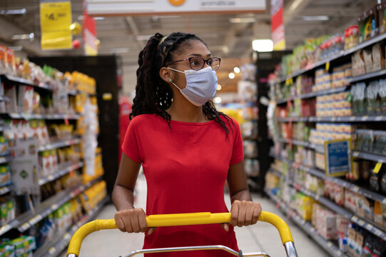 Afro latina young woman wearing a face mask pushes shopping cart through supermarket aisle