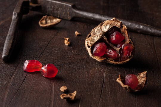 Still life composition with ripe red pomegranate seeds arranged in walnut shells on dark wooden background