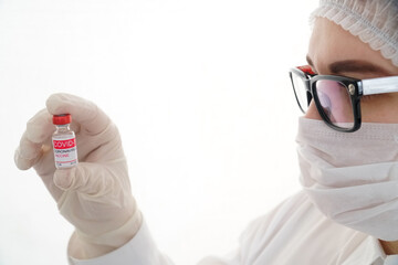 Close up of young female doctor holding and looking at a glass bottle of coronavirus vaccine. Concept of coronavirus vaccination