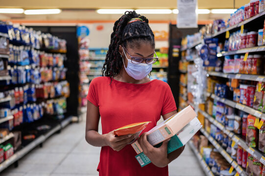 Afro latina young woman wearing a face mask walks aisle and looks at products while shopping in supermarket
