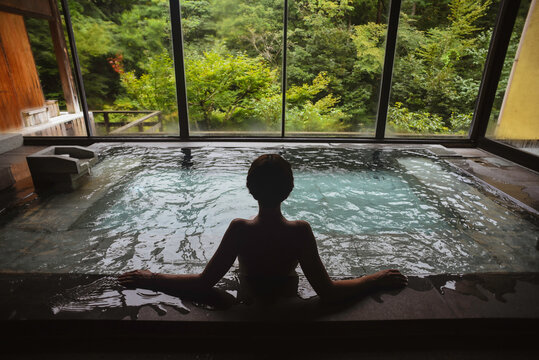 Silhouette of young caucasian woman enjoying.a relaxing thermal waters bath at a traditional Japanese onsen ryokan, view from behind