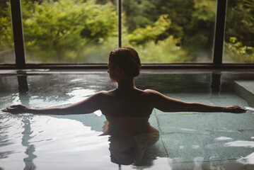 Silhouette of young caucasian woman enjoying.a relaxing thermal waters bath at a traditional Japanese onsen ryokan, view from behind