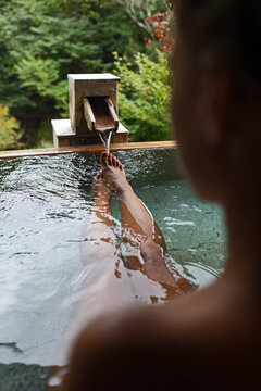 Legs and feet of caucasian female traveler enjoying a thermal waters bath in Japanese onsen, view from behind