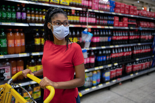 Afro latina young woman wearing a face mask looks at products in beverage aisle while shopping in supermarket