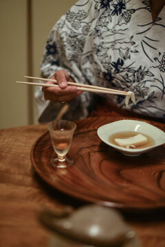Close up view of hands of female caucasian woman in kimono using chopsticks to eat Japanese food at ryokan