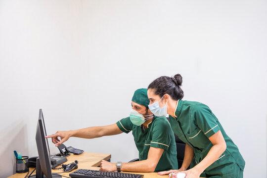 Focused female doctor frowning and thinking while standing near male coworker and reading data from computer in lab of modern hospital using face mask during coronavirus pandemic