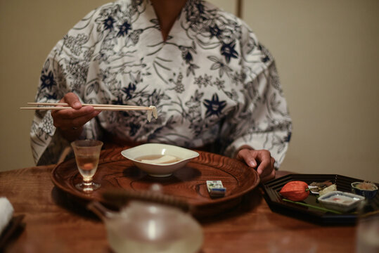 Close up view of hands of female caucasian woman in kimono using chopsticks to eat Japanese food at ryokan