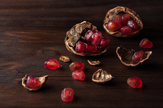 Top view still life composition with ripe red pomegranate seeds arranged in walnut shells on dark wooden background