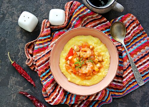 Homemade shrimp and grits with smoked sausages, sweet red peppers, onions and cheese in a pink bowl on a dark concrete background. American cuisine. Recipes with corn grits.