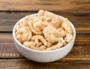 Fried pork cracklings on a white bowl over wooden table