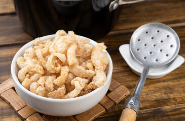 Fried pork cracklings on a white bowl over wooden table