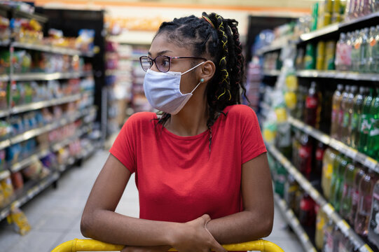 Afro Latina Young Woman Wearing A Face Mask Pushes Shopping Cart Through Supermarket Aisle